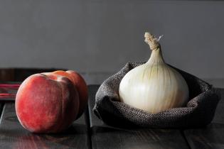 one peach and one onion against a gray background